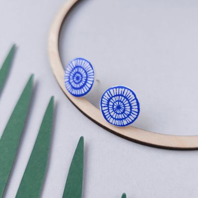 A pair of blue and white polymer clay stud earrings with a circular design. The earrings are placed on a wooden arch.
