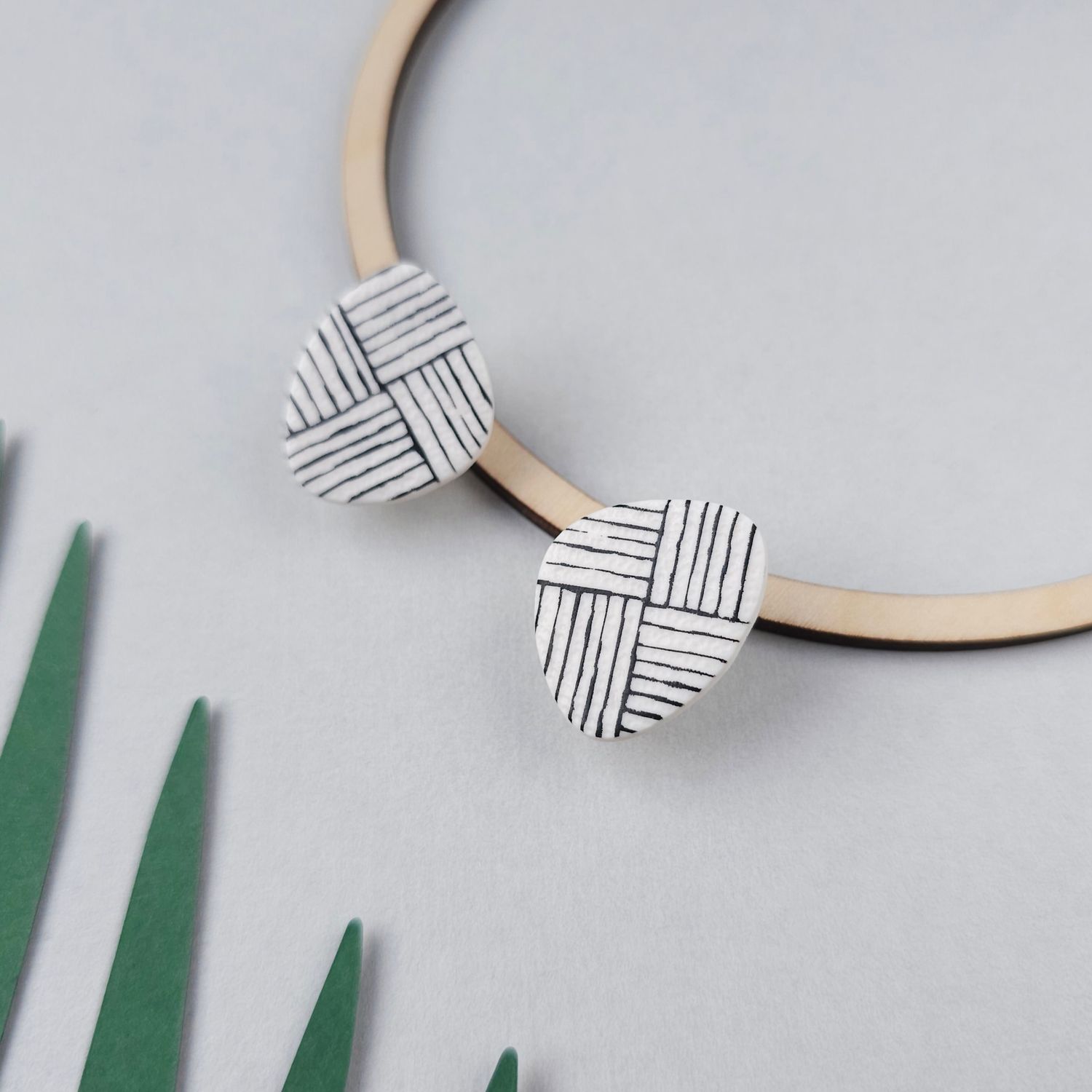 A pair of white polymer clay earrings with a black geometric pattern. 