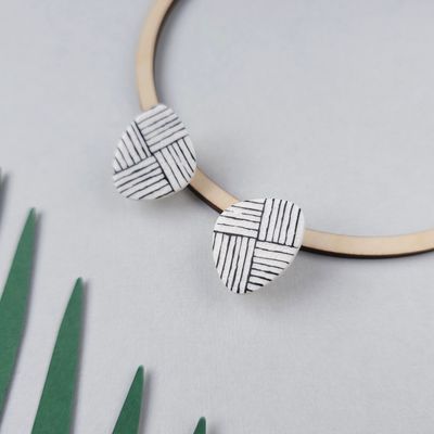 A pair of white polymer clay earrings with a black geometric pattern. 