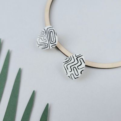 A white polymer clay pair of earrings with a black geometric pattern, and are shaped like an organic teardrop blob.