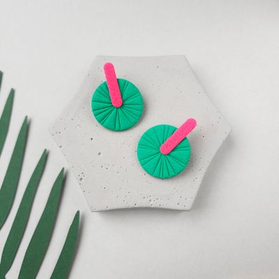 A pair of green and pink statement earrings that are round and have a textured surface. 