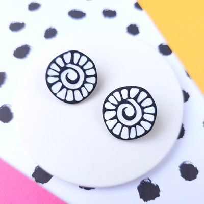 A pair of polymer clay circle stud earrings that are round and have a white mosaic spiral design on a black background.