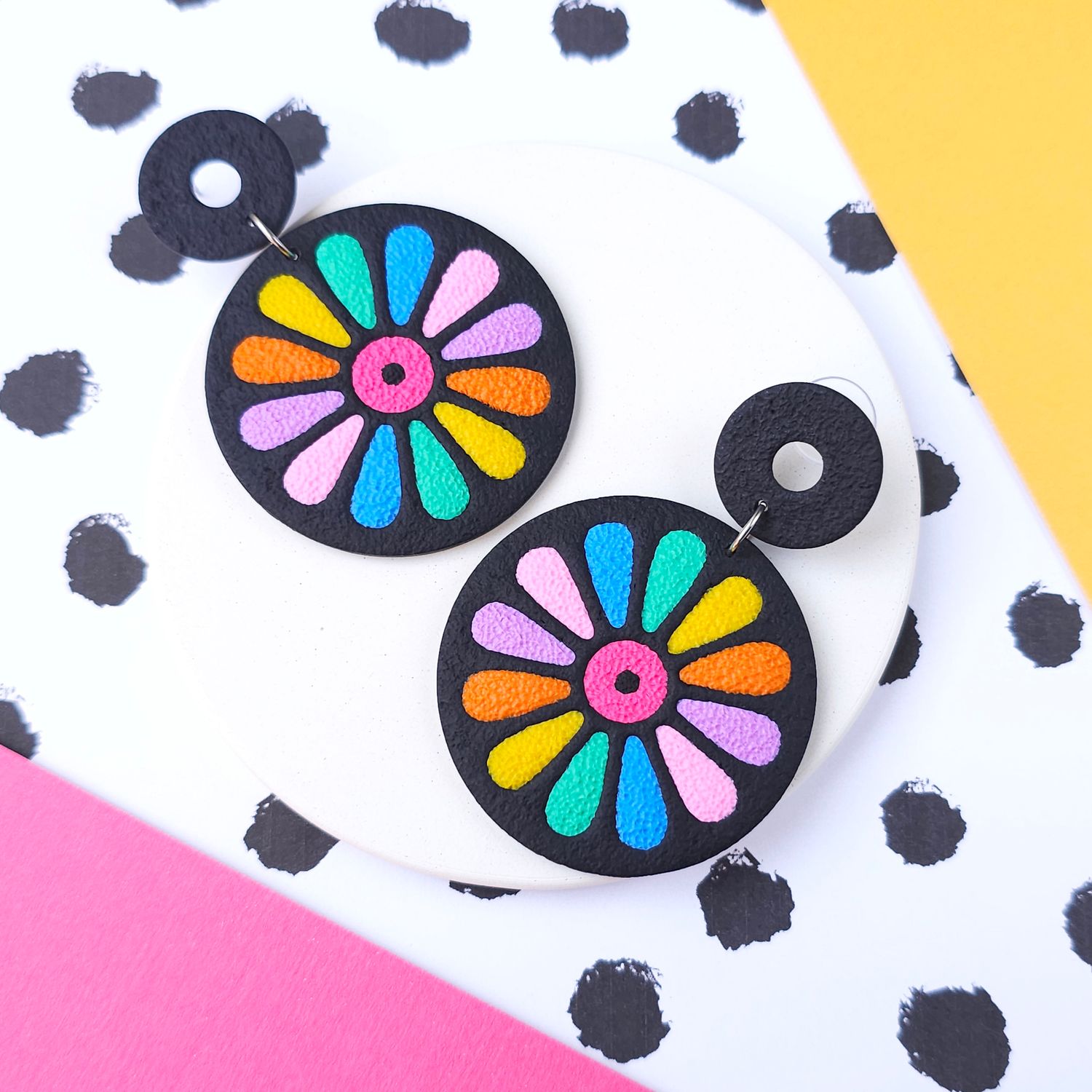 A pair of colourful flower-shaped earrings with a black background.