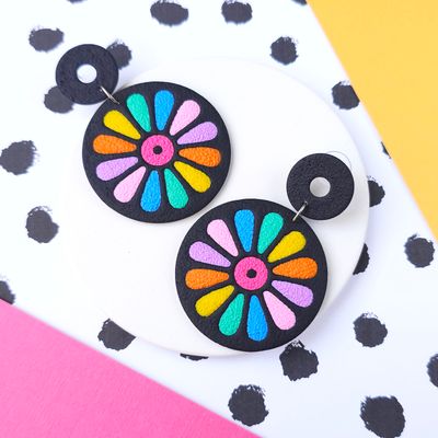 A pair of colourful flower-shaped earrings with a black background.
