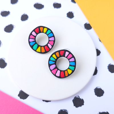 A pair of rainbow coloured circle hoop earrings with a black background.