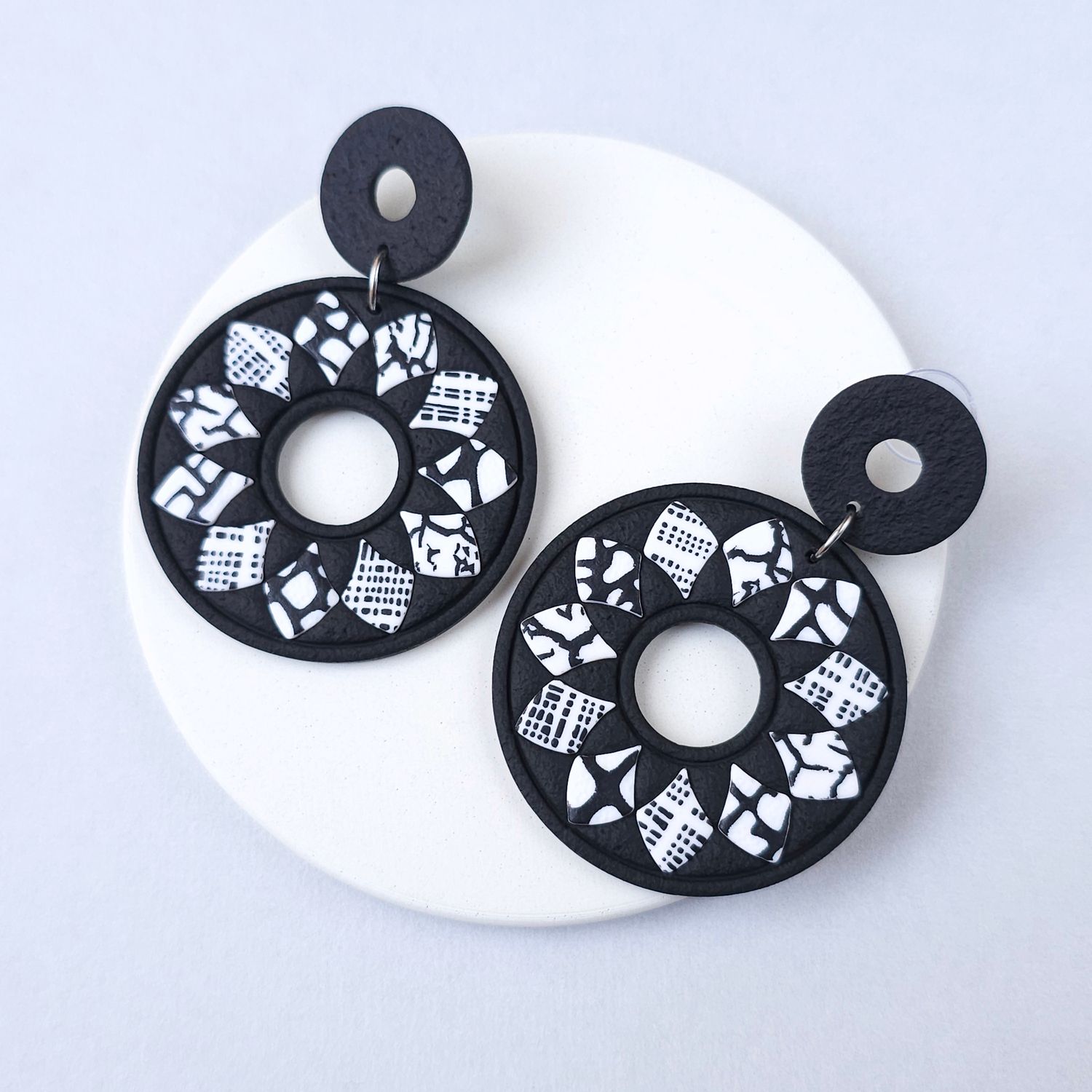 Black and white patterned earrings with a large, round shape. that are made of polymer clay and have a geometric design