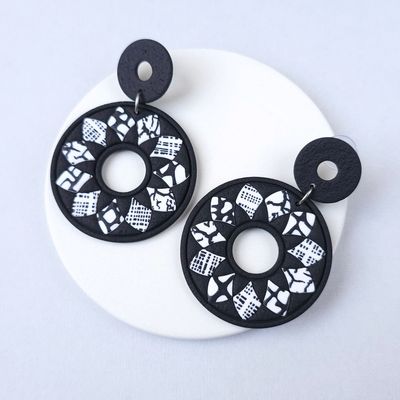 Black and white patterned earrings with a large, round shape. that are made of polymer clay and have a geometric design