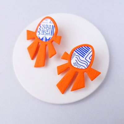 A pair of orange statement earrings with a white and blue geometric pattern.
