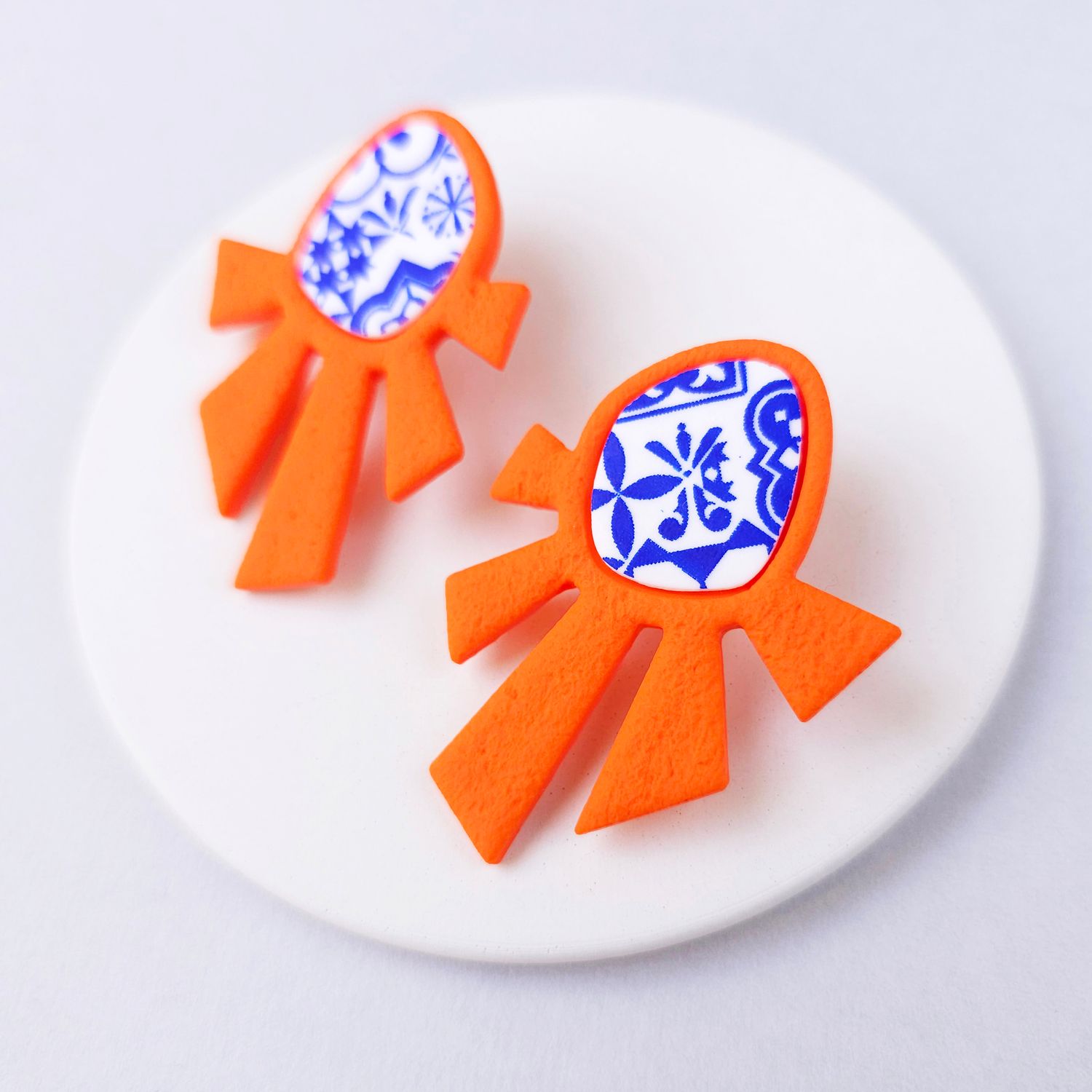 A pair of orange and blue statement earrings with a geometric design.