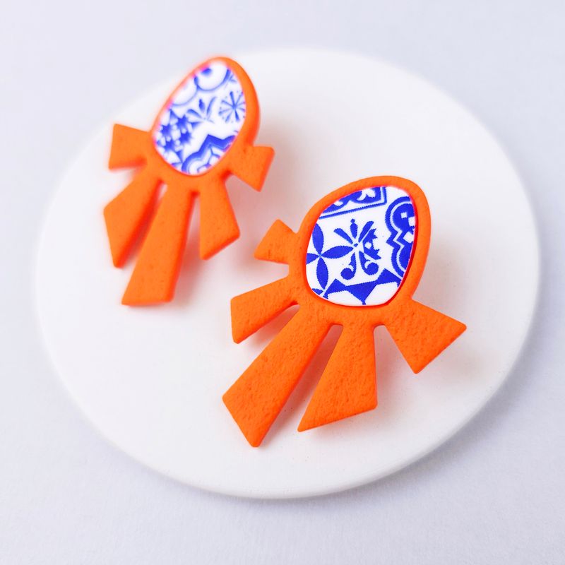 A pair of orange and blue statement earrings with a geometric design.