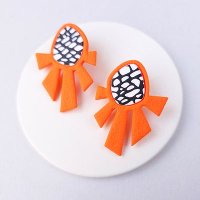 A pair of orange geometric earrings with a black and white patterned design.