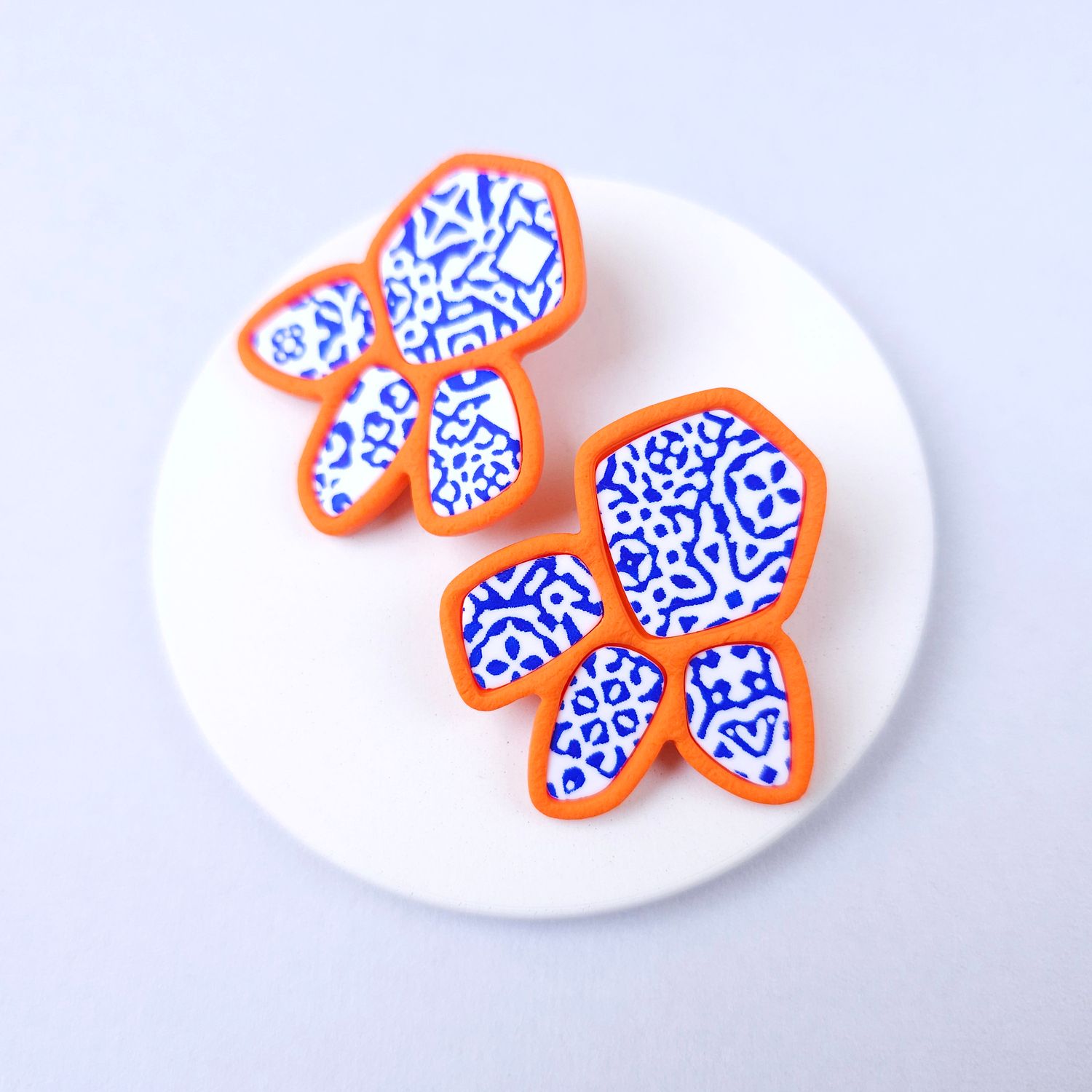 Two organic-shaped earrings with a white and blue patterned design, outlined in orange.