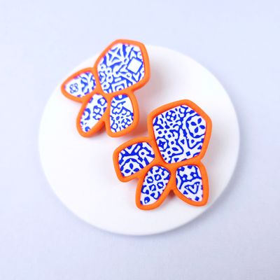 Two organic-shaped earrings with a white and blue patterned design, outlined in orange.