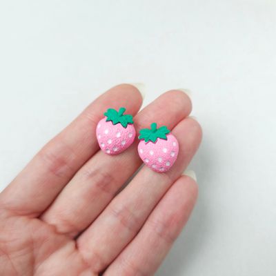 Two small, light pink, strawberry-shaped stud earrings with white seeds and green top leaves.