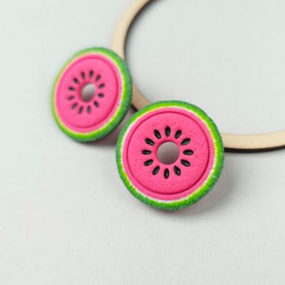 Two watermelon-shaped polymer clay earrings with pink centres, black seed details, and green and white edges.