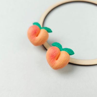 Two peach-shaped textured earrings with green leaves handcrafted from polymer clay.