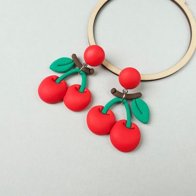 A pair of bright red big cherry earrings with green leaves and brown stems. 