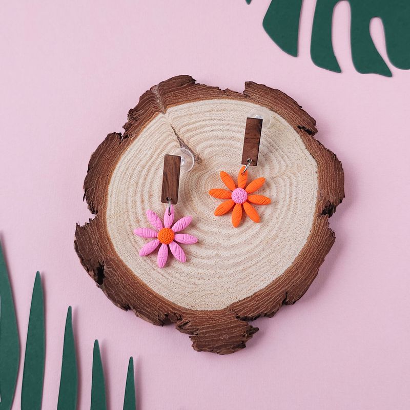 Two daisy earrings, one pink and one orange, with a wooden rectangular top.