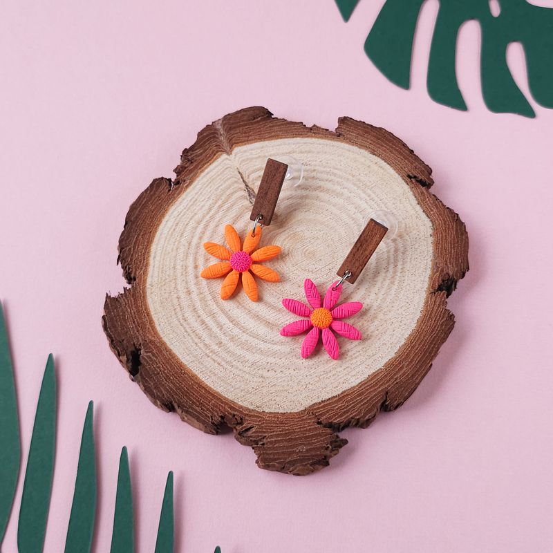 A pair of daisy earrings featuring orange and pink flower designs. Each earring has a dark brown rectangular wooden stud.