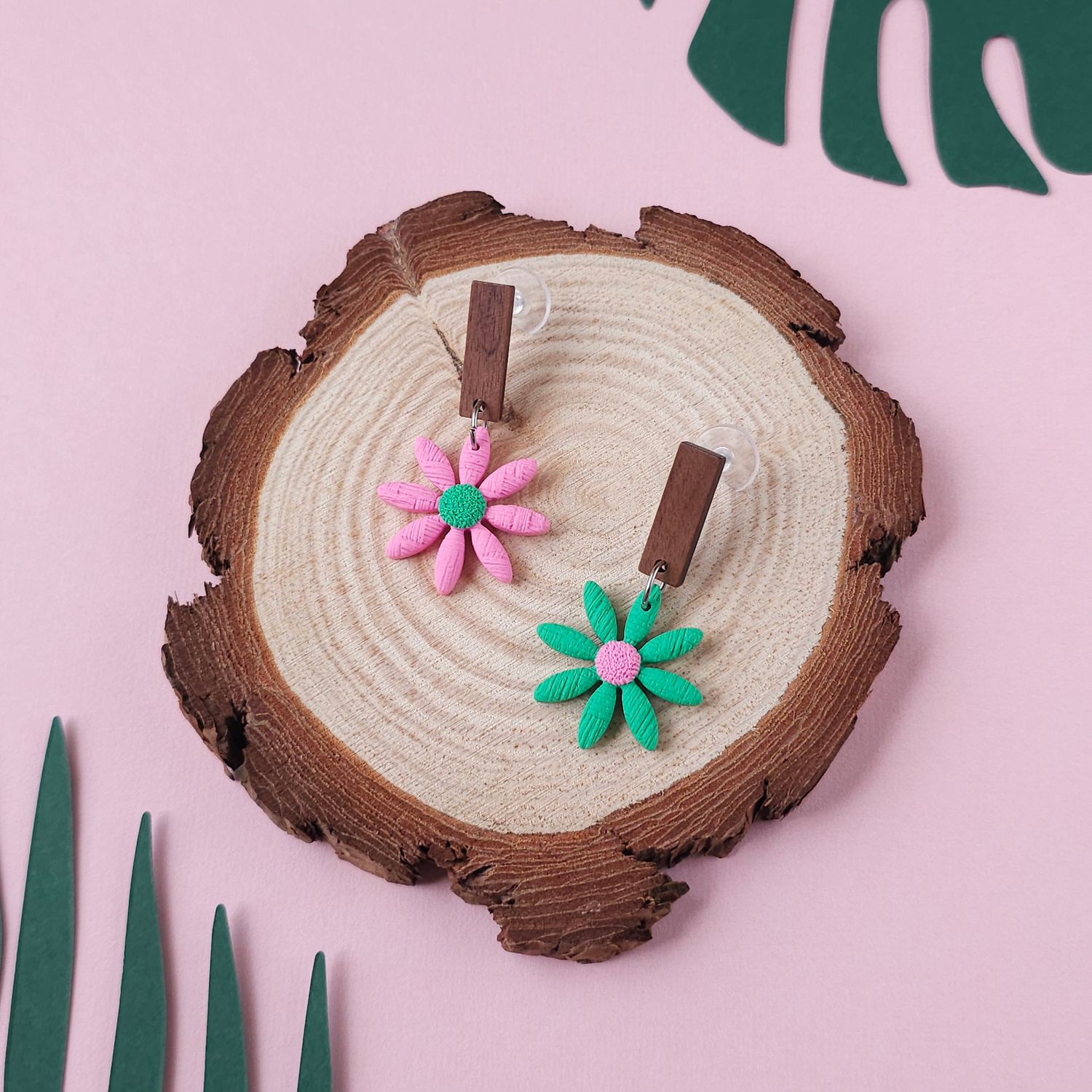 A pair of daisy earrings, one light pink with a green centre, another one green with a light pink centre.