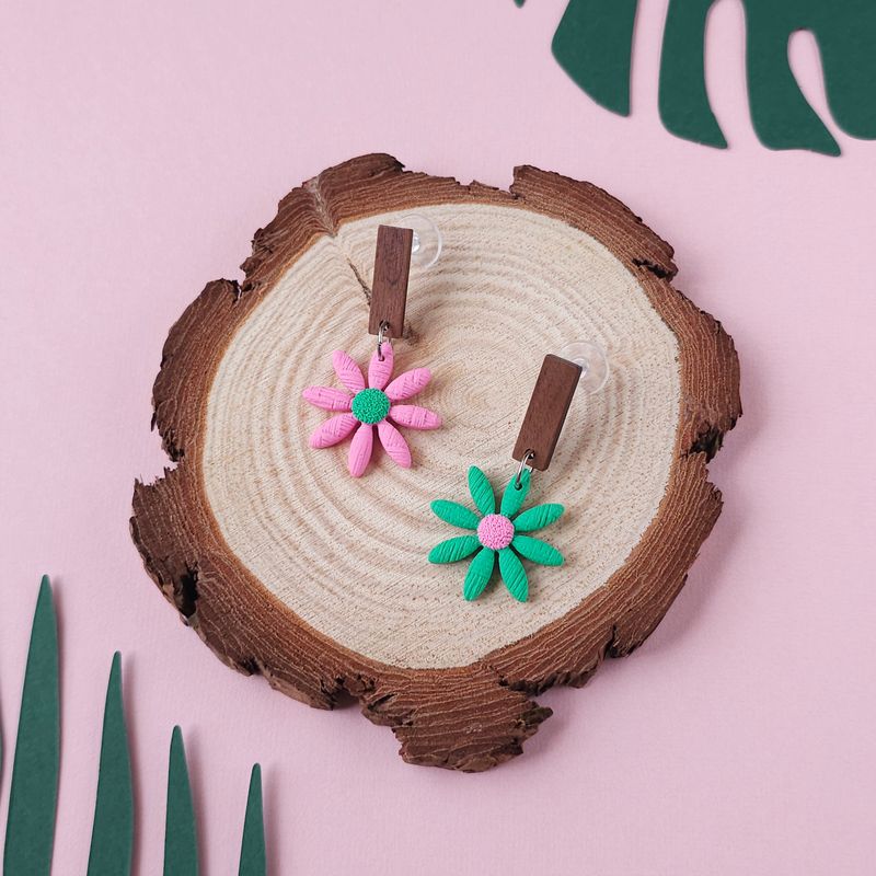 A pair of daisy earrings, one light pink with a green centre, another one green with a light pink centre.