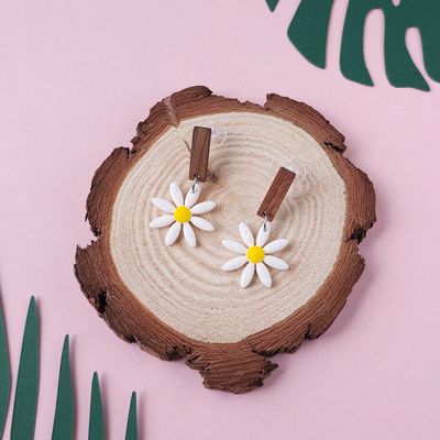A pair of daisy earrings, with a yellow centre, hanging from small, rectangular, dark wooden studs.