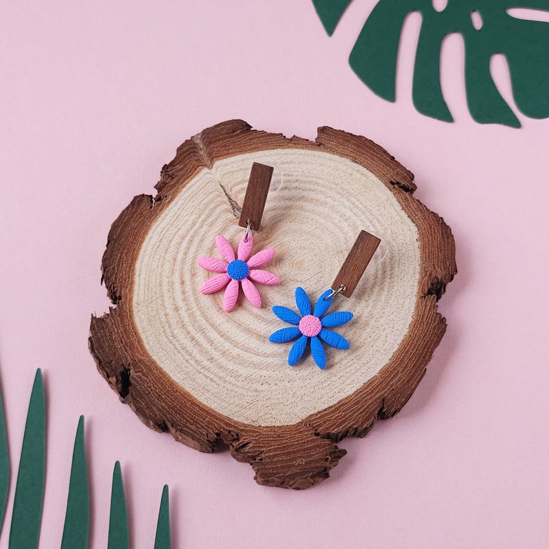 A pair of daisy earrings, one pink with a blue centre and one blue with a pink centre.