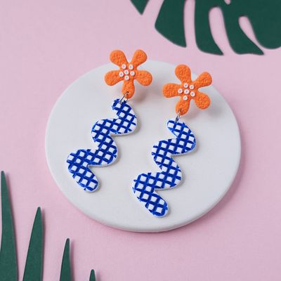 A pair of orange flower earrings with white detailing and blue and white patterned, wavy drops.