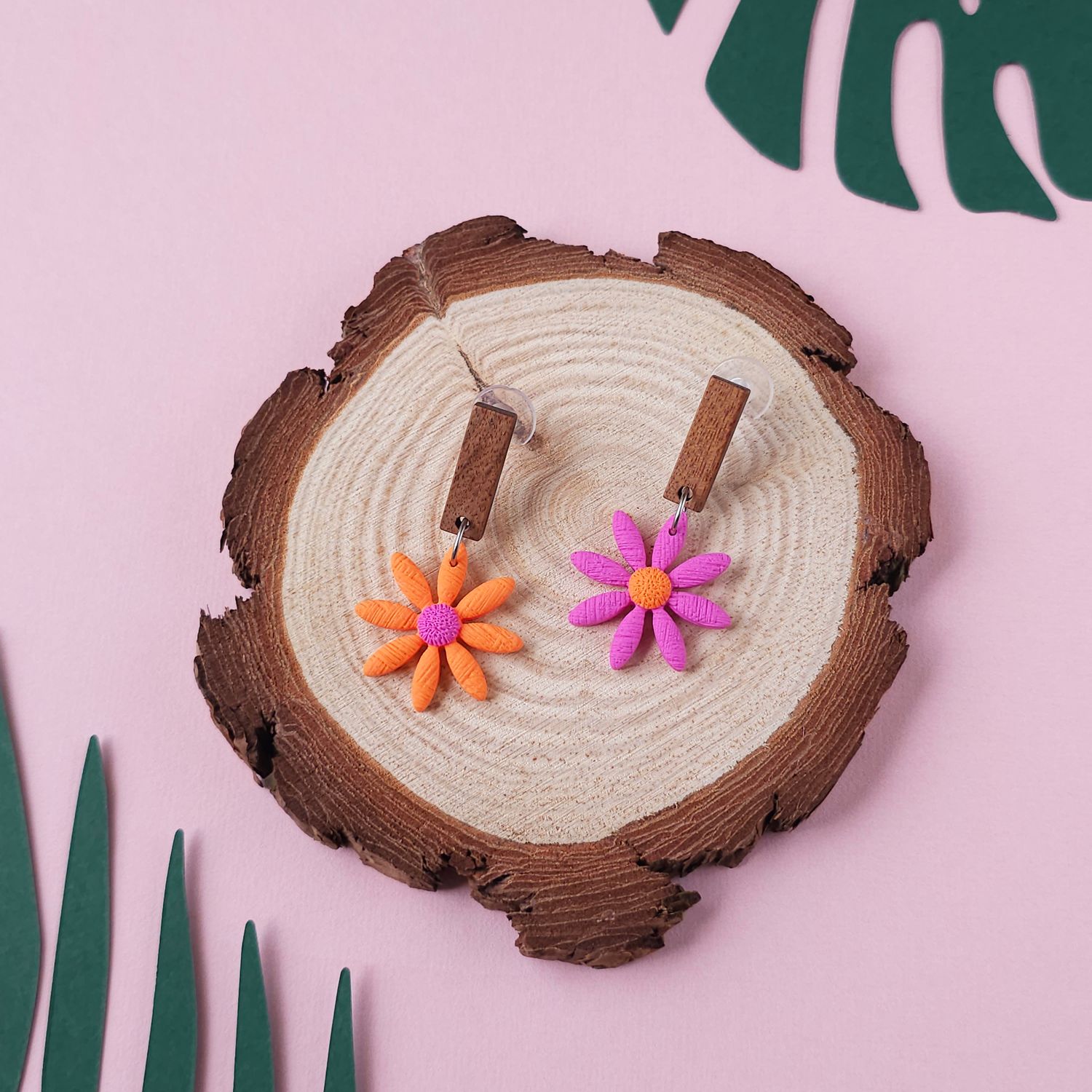 Two daisy earrings, one orange with a purple centre and one purple with an orange centre.