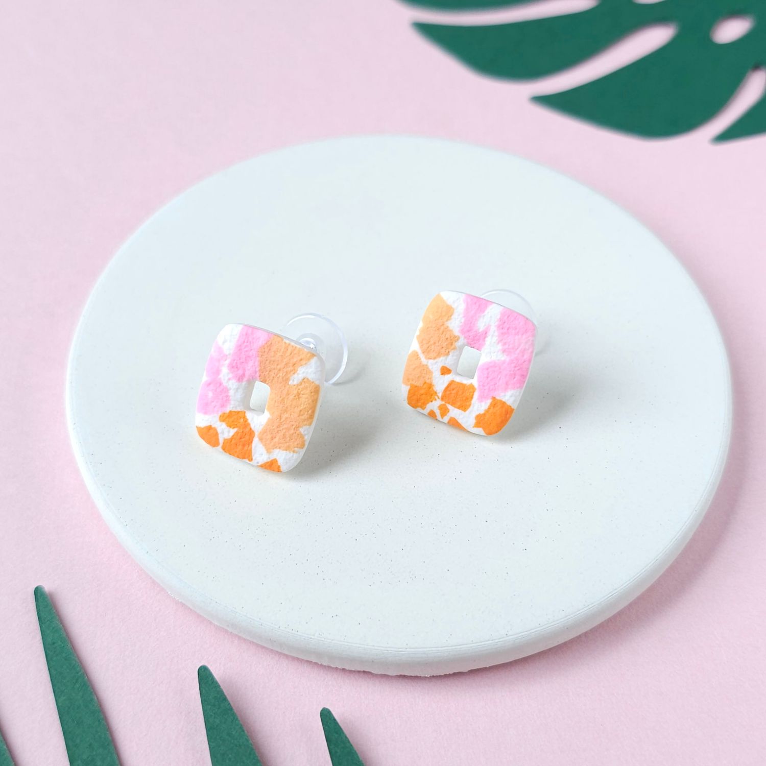 A pair of small rectangular stud earrings with a colourful, terrazzo design in pink, orange and white.