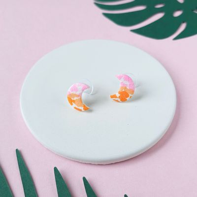 A pair of crescent moon stud earrings. The earrings have a speckled design in pink, orange, and white.