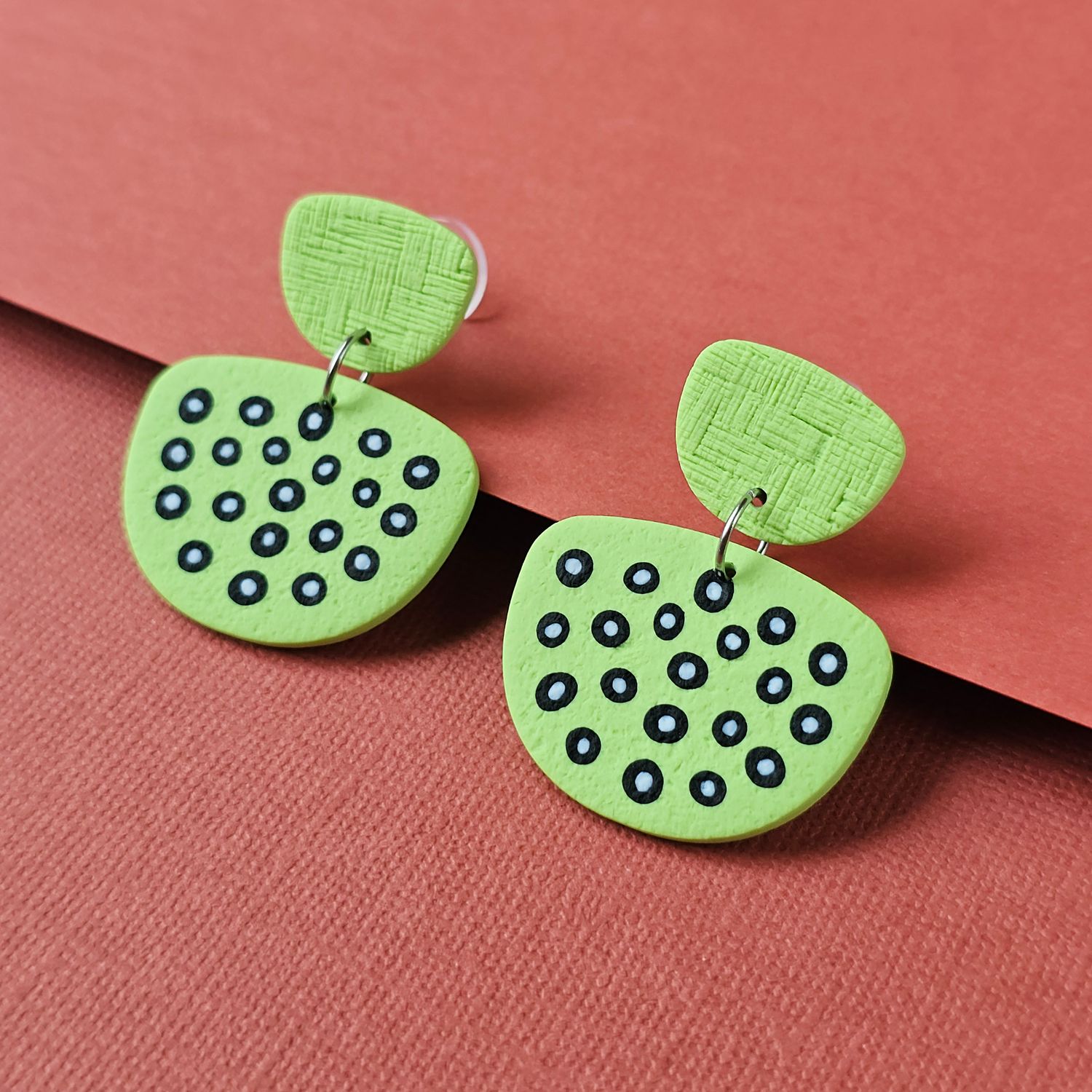 Lime green earrings that feature a textured top piece and a rounded bottom piece with black and white dot patterns.