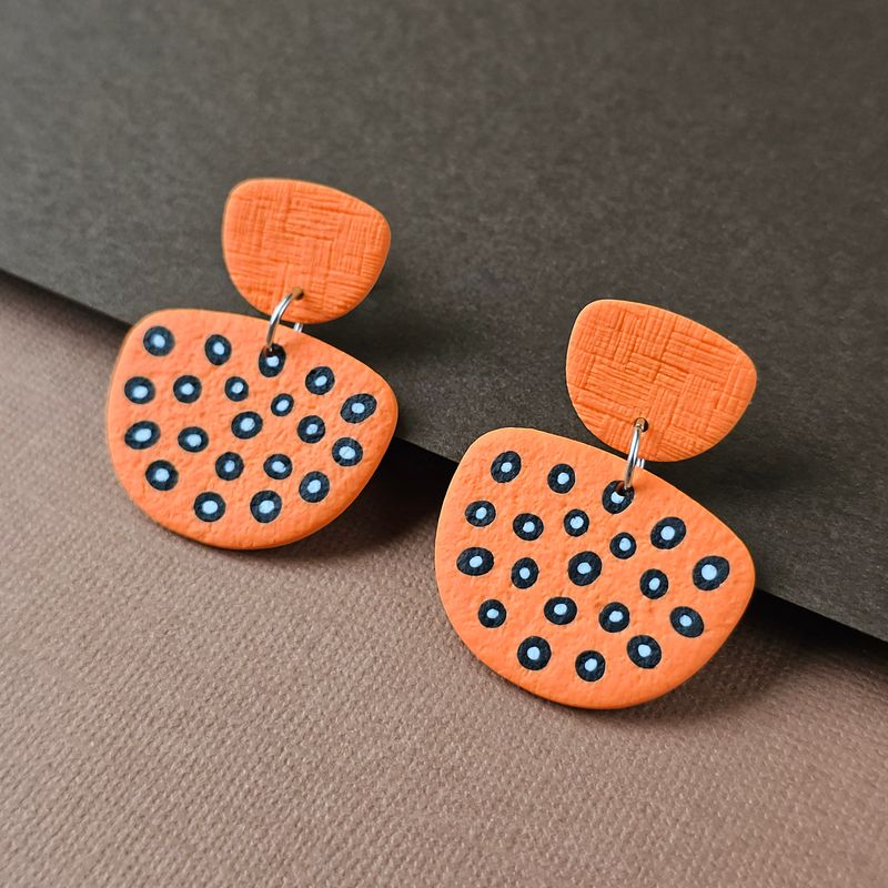 A pair of earrings that has a small top and a larger, irregular shape below, decorated with black and white dot patterns.