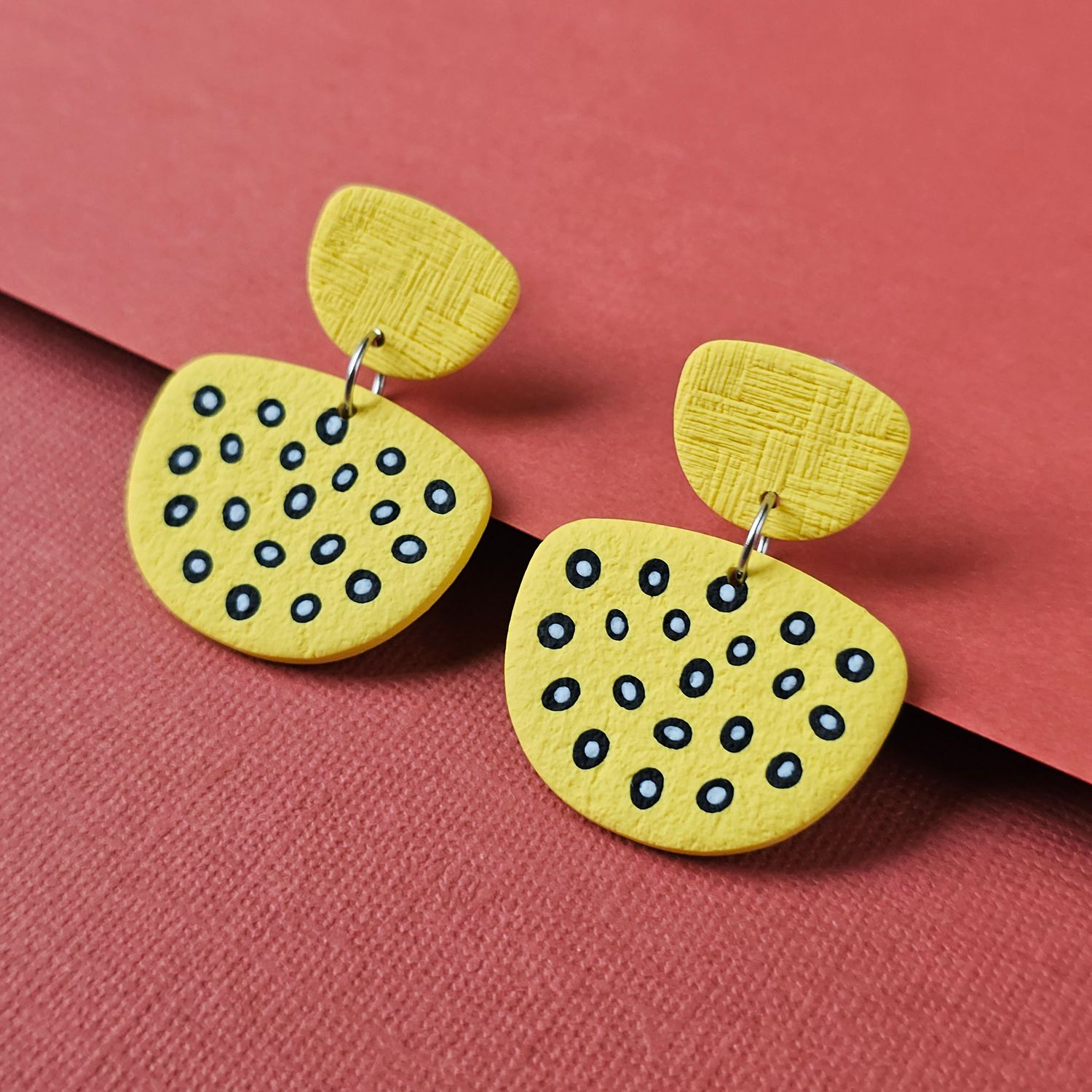 Yellow geometric earrings with black dot details.