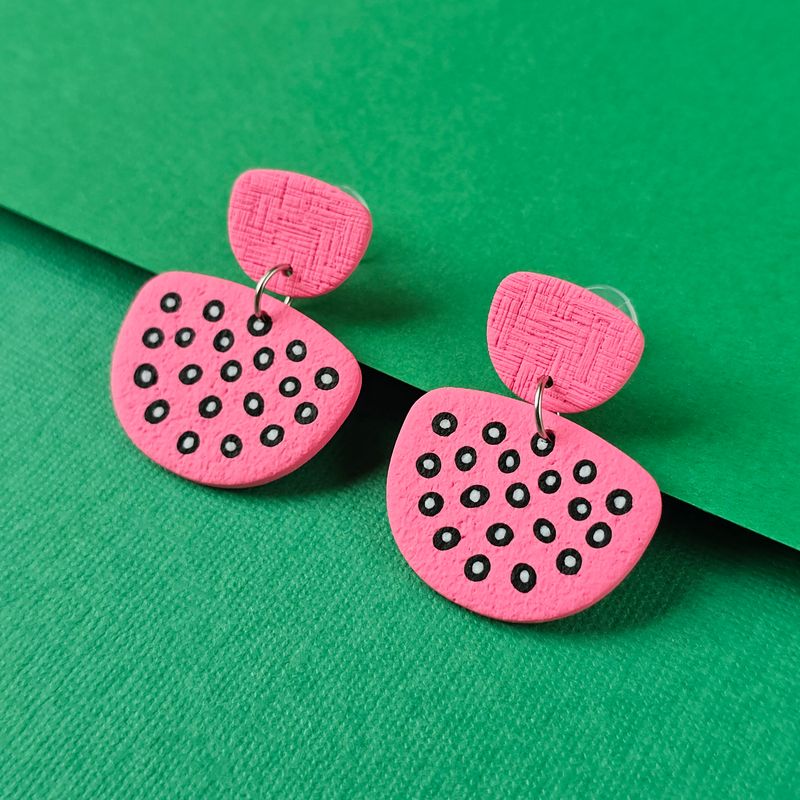 A pair of pink earrings, with a textured, oval top and a larger, irregular shape below, decorated with black circles