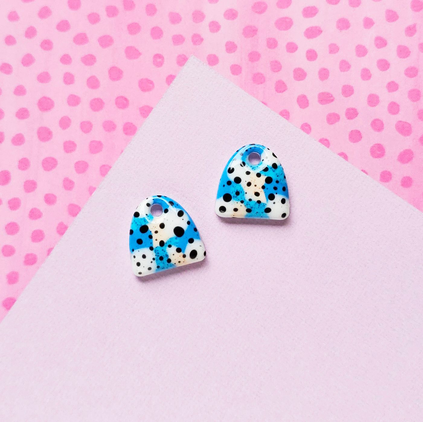 Two abstract charm resin earrings in white, blue, and black, each with a hole at the top.