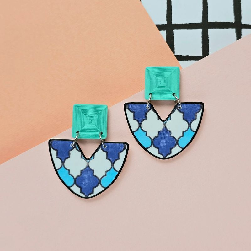 A picture showing a large pair of earrings with a geometric blue/white tile print and an aqua blue textured upper square bead