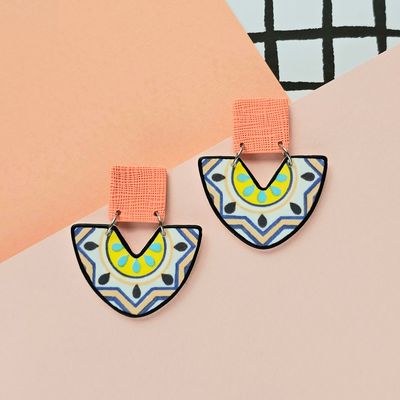 A picture showing a large pair of earrings that have a summer tile print and an orange, textured upper square bead.