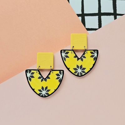 A picture showing a pair of yellow and dark blue tile earrings with a black outline on the bottom bead.