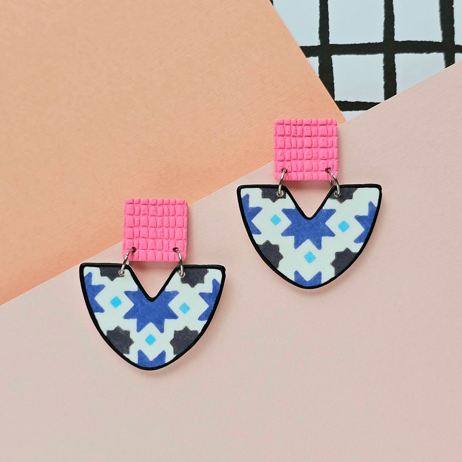 A picture showing a pair of pink and blue tile earrings with a black outline for the bottom bead.