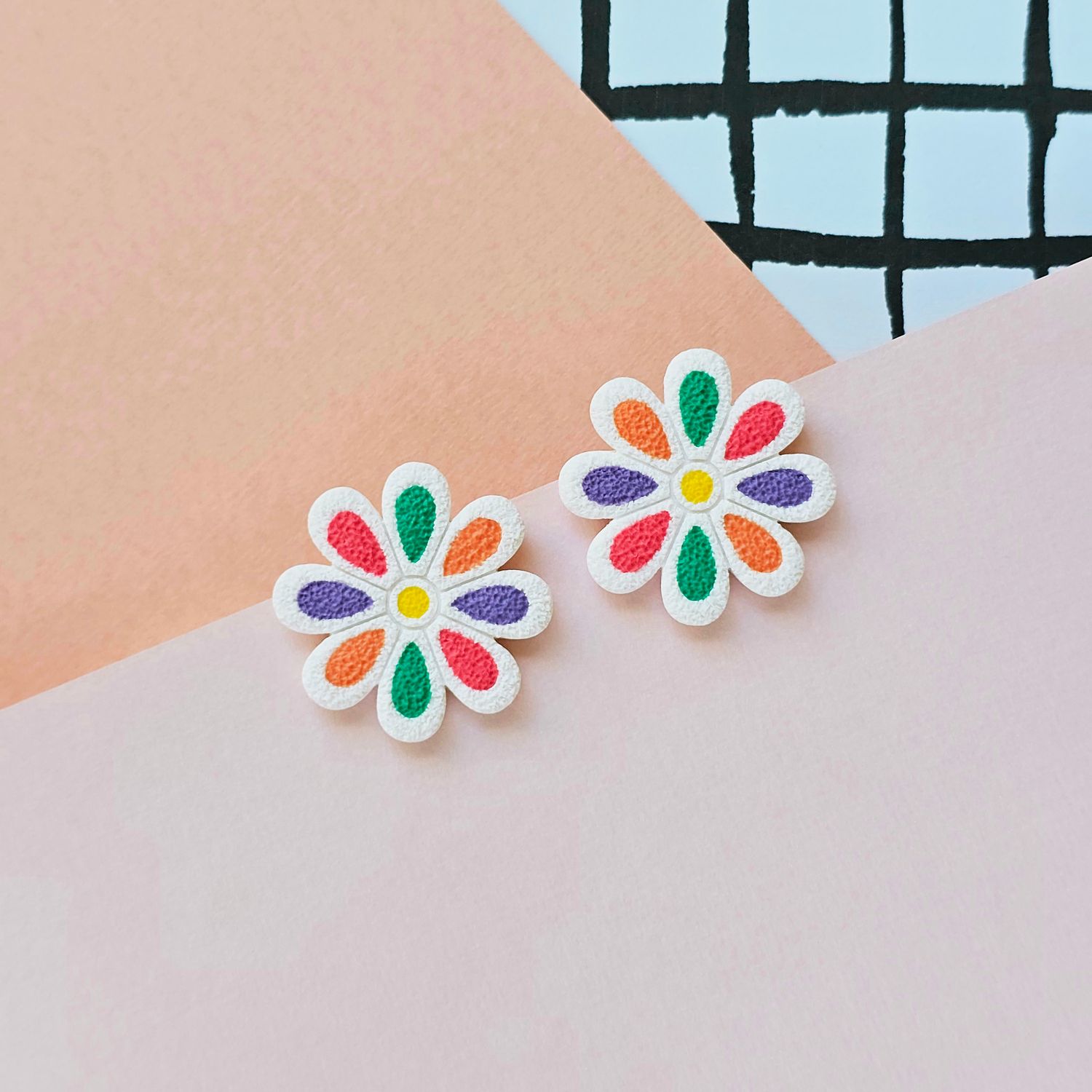 A pair of floral earrings with orange, purple, pink and green petals enclosed in a white base.