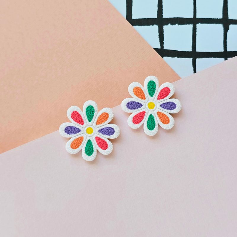 A pair of floral earrings with orange, purple, pink and green petals enclosed in a white base.
