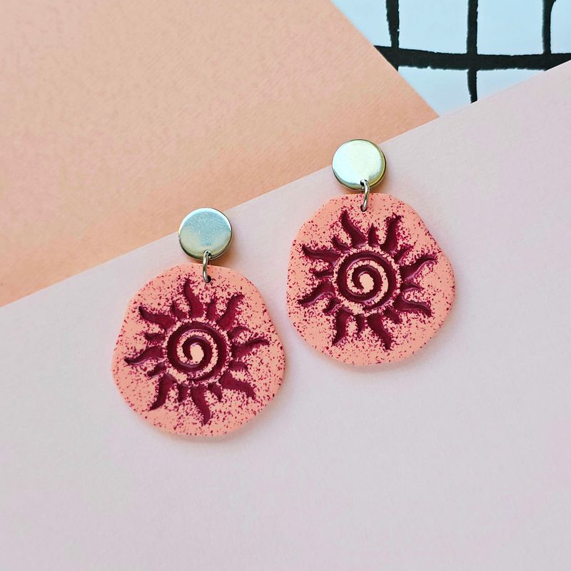 A pair of dark red sun earrings in a tribal style.