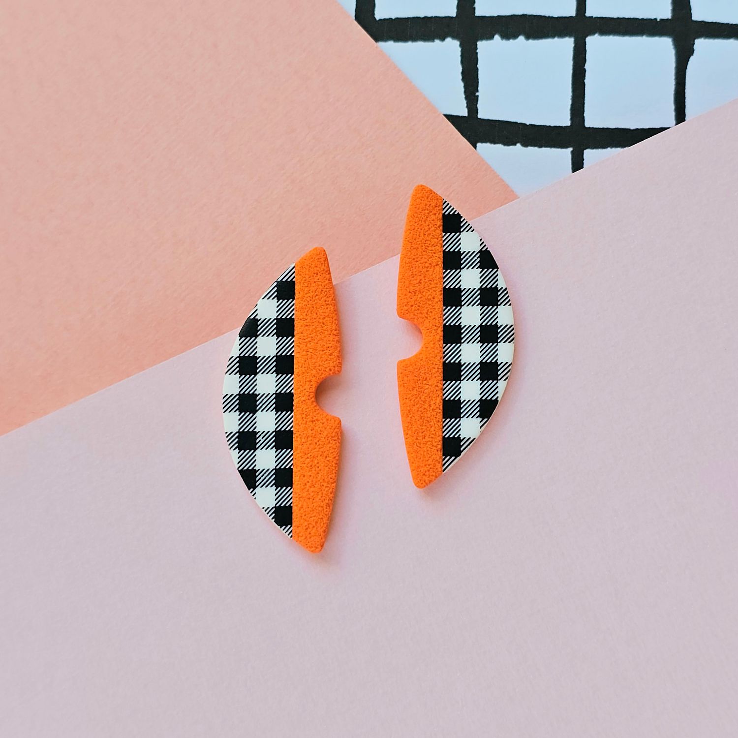 A pair of orange and gingham pattern semicircle polymer clay earrings.