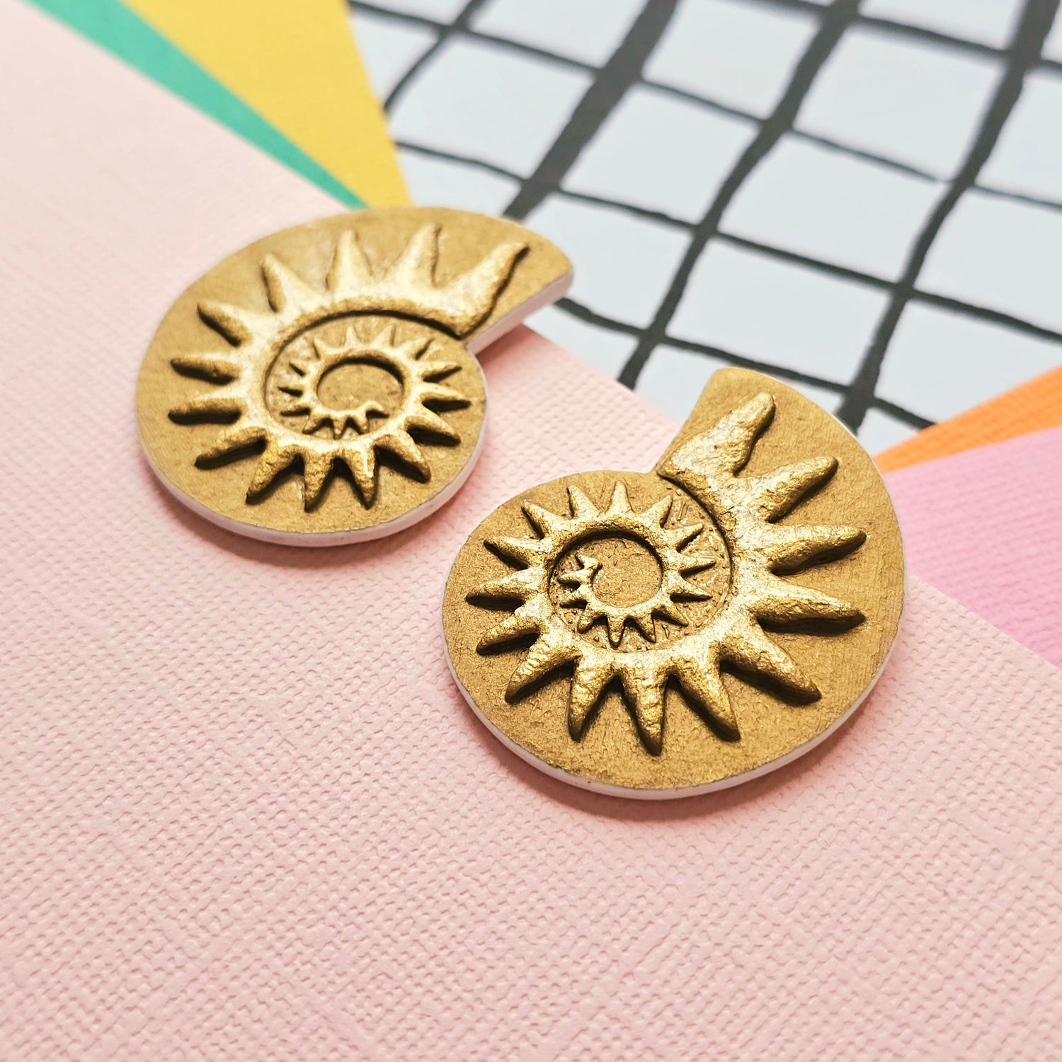 A close up of a pair of rich gold coloured spiral faux ammonite polymer clay earrings.