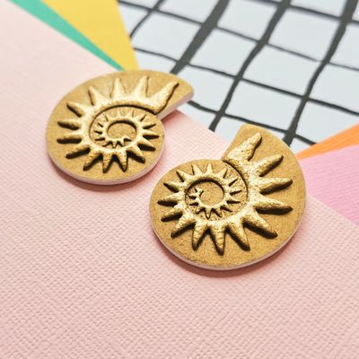 A close up of a pair of rich gold coloured spiral faux ammonite polymer clay earrings.