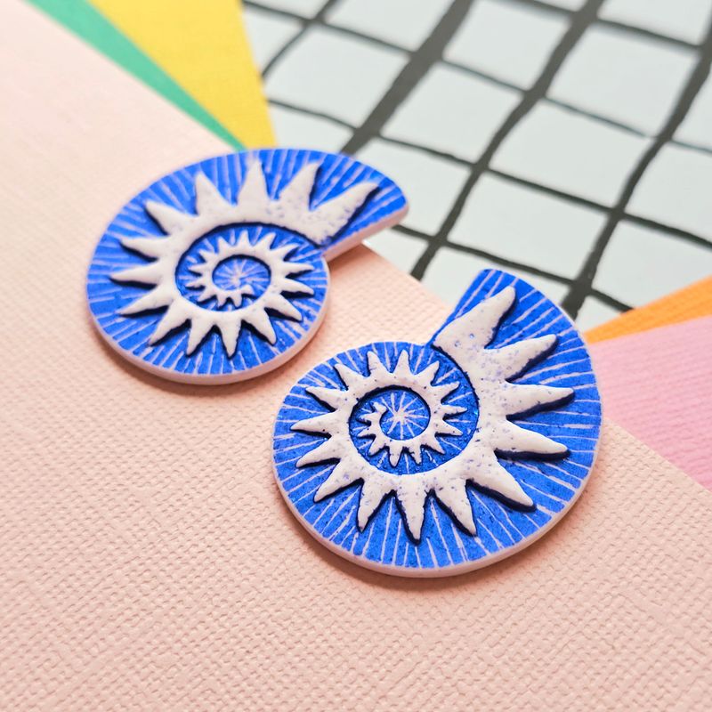A close up of a pair of blue and white spiral faux ammonite polymer clay earrings.