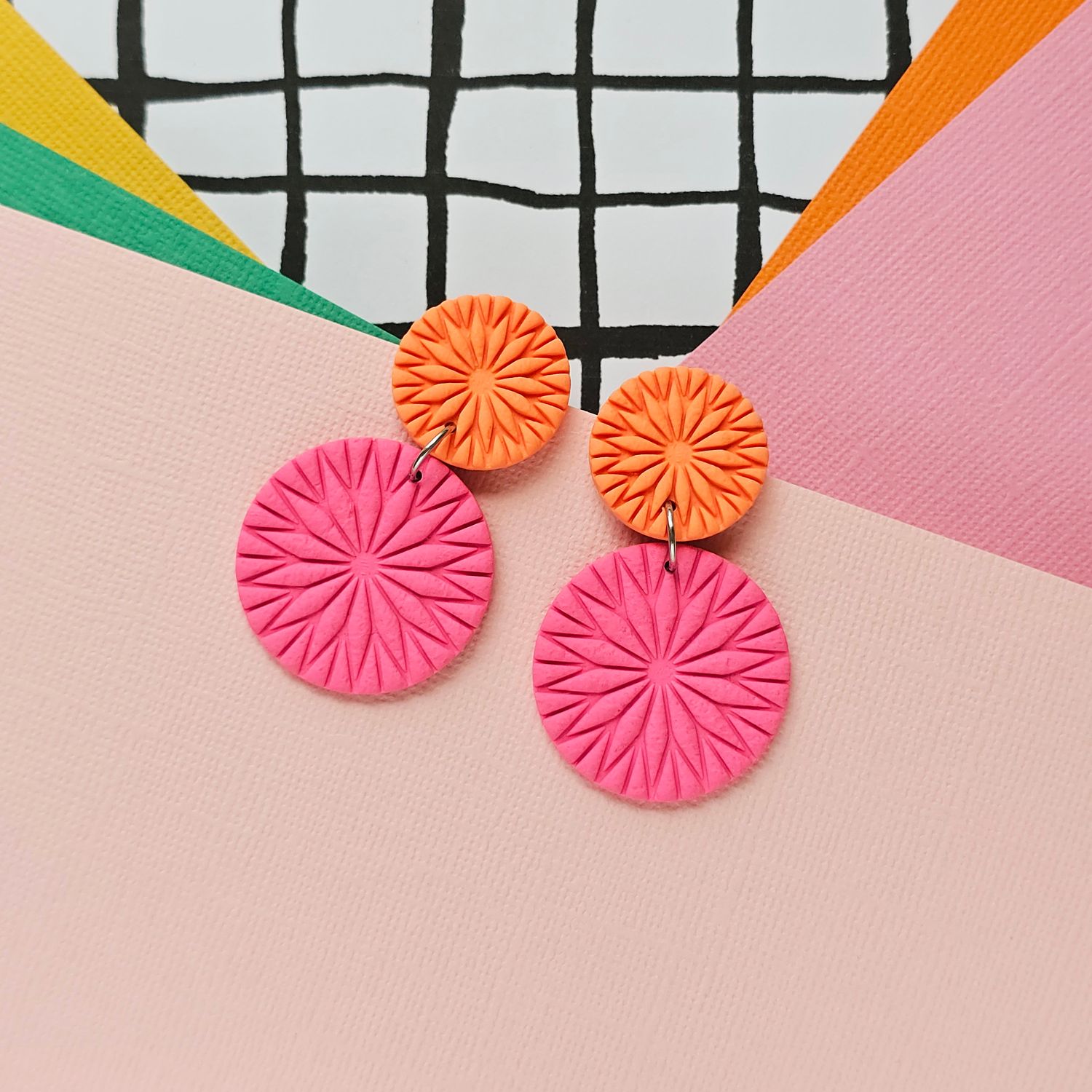A pair of orange and pink textured round polymer clay earrings.