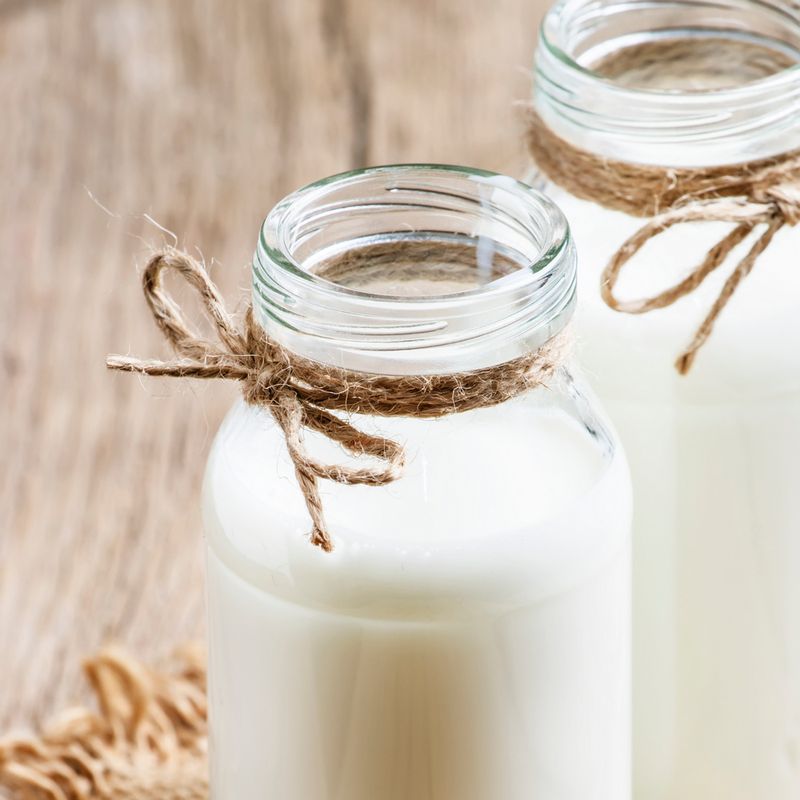 A2A2 Half and half For Pets- Two clear glass bottles of A2A2 Half and Half, tied with rustic twine bows, on a light brown wooden surface.