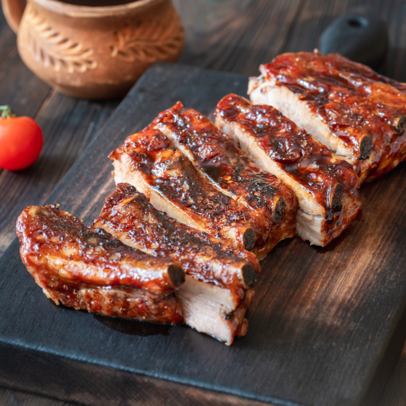 Country Style Ribs Grilled Country Style Ribs, glistening with dark BBQ sauce, sliced on a dark wood board, with a red tomato and traditional po